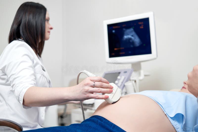Doctor de sexo femenino que usa ultrasonido y defendiendo a la mujer embarazada imagen de archivo libre de regalías Doctor de sexo femenino que usa ultrasonido y defendiendo a la mujer embarazada imagen de archivo libre de regalías