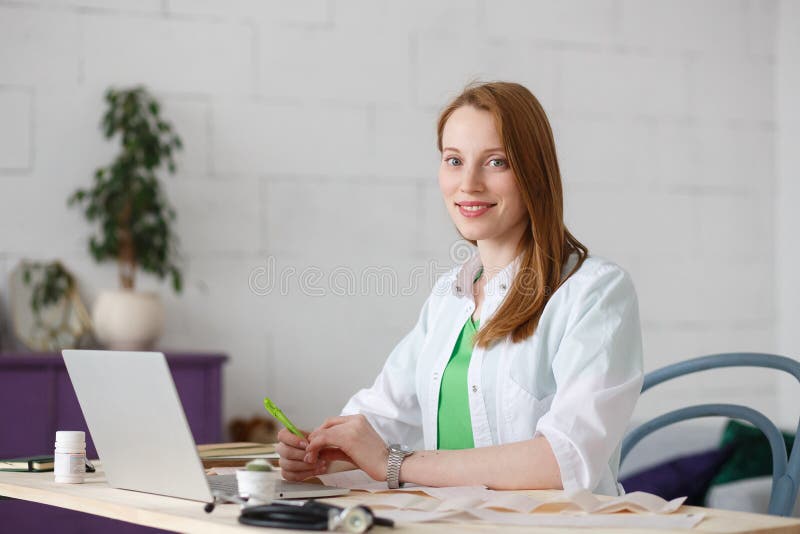 Doctor de sexo femenino sonriente de los jóvenes hermosos que se sienta en el escritorio imagen de archivo Doctor de sexo femenino sonriente de los jóvenes hermosos que se sienta en el escritorio imagen de archivo