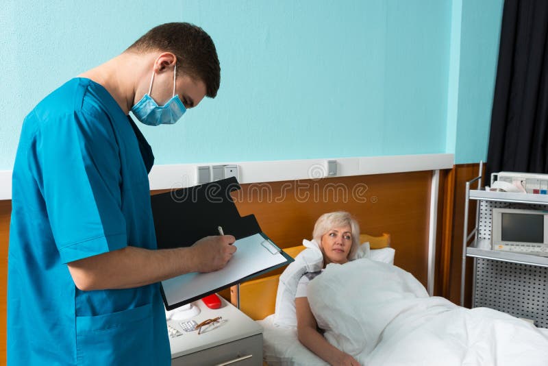 Doctor de sexo masculino en el uniforme que lleva una máscara que hace algunas notas en repor fotografía de archivo Doctor de sexo masculino en el uniforme que lleva una máscara que hace algunas notas en repor fotografía de archivo