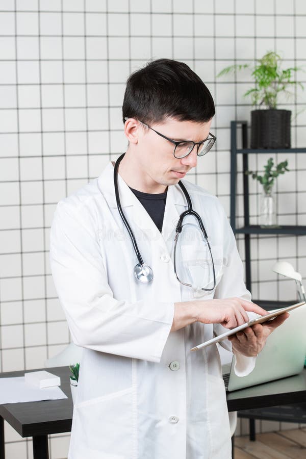 Doctor de sexo masculino joven hermoso pensativo usando la tableta Tecnologías en concepto de la medicina fotografía de archivo libre de regalías Doctor de sexo masculino joven hermoso pensativo usando la tableta Tecnologías en concepto de la medicina fotografía de archivo libre de regalías