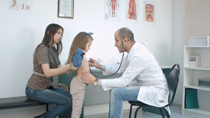 Doctor de sexo masculino que escucha el pecho de la muchacha con el estetoscopio en su oficina imagen de archivo libre de regalías Doctor de sexo masculino que escucha el pecho de la muchacha con el estetoscopio en su oficina imagen de archivo libre de regalías