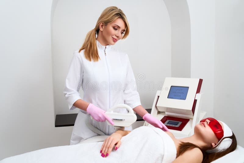 Doctor del cosmetólogo que hace la depilación del retiro del pelo de los elos en las manos atractivas de la mujer joven en salón fotografía de archivo Doctor del cosmetólogo que hace la depilación del retiro del pelo de los elos en las manos atractivas de la mujer joven en salón fotografía de archivo