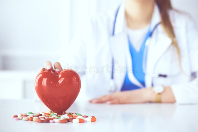 Doctor en la capa blanca con el estetoscopio que lleva a cabo las píldoras y el corazón plástico aislados en blanco imagen de archivo Doctor en la capa blanca con el estetoscopio que lleva a cabo las píldoras y el corazón plástico aislados en blanco imagen de archivo