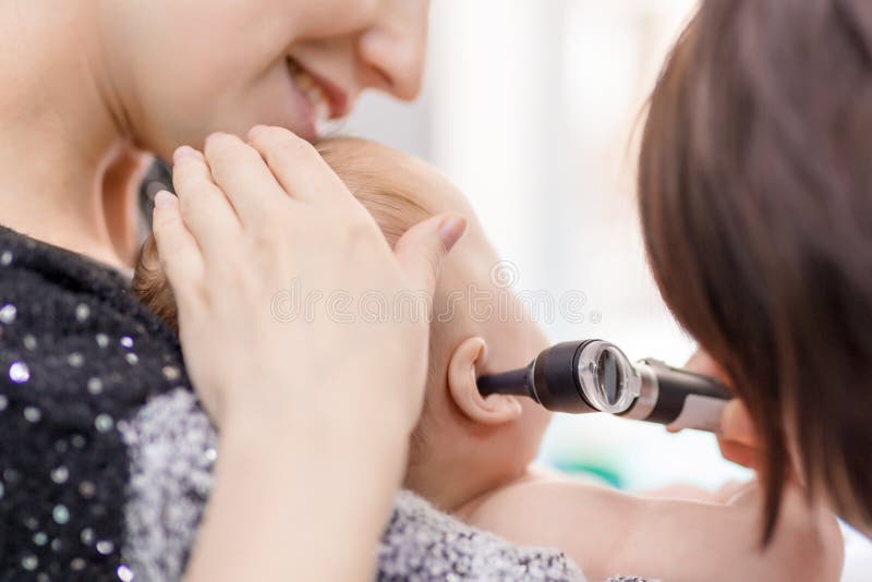 Doctor examining childs ear with otoscope. Mom holding baby with hands. Children healthcare and disease prevention