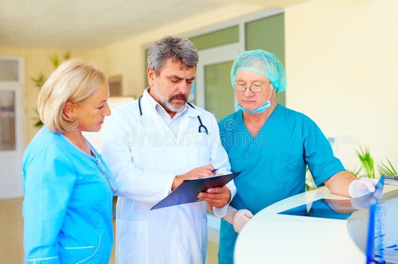 Doctor experimentado y personal médico que consultan sobre historial médico en hospital imagenes de archivo Doctor experimentado y personal médico que consultan sobre historial médico en hospital imagenes de archivo