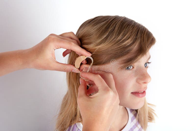 Doctor fitting a young girl patient with hearing aid