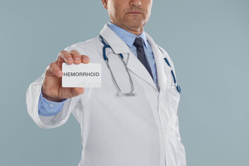 Doctor holding business card with word HEMORRHOID on grey background, closeup stock photography Doctor holding business card with word HEMORRHOID on grey background, closeup stock photography