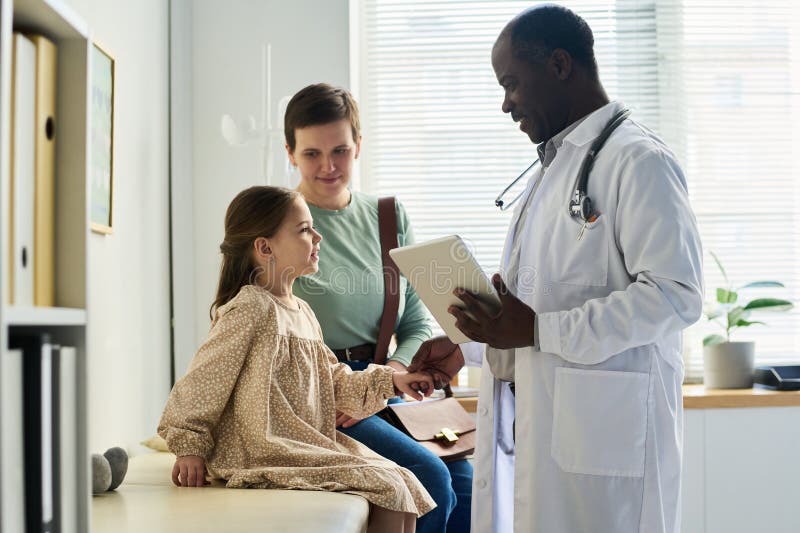 Doctor Interacting with Child Patient and Parent in Clinic stock photography