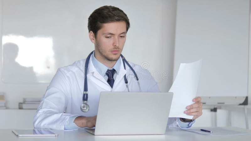 Doctor joven Working On Laptop y documentos médicos