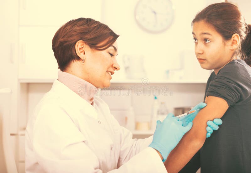 Doctor makes injection girl. Doctor in white gown does injection to girl in procedural office of hospital stock photo Doctor makes injection girl. Doctor in white gown does injection to girl in procedural office of hospital stock photo
