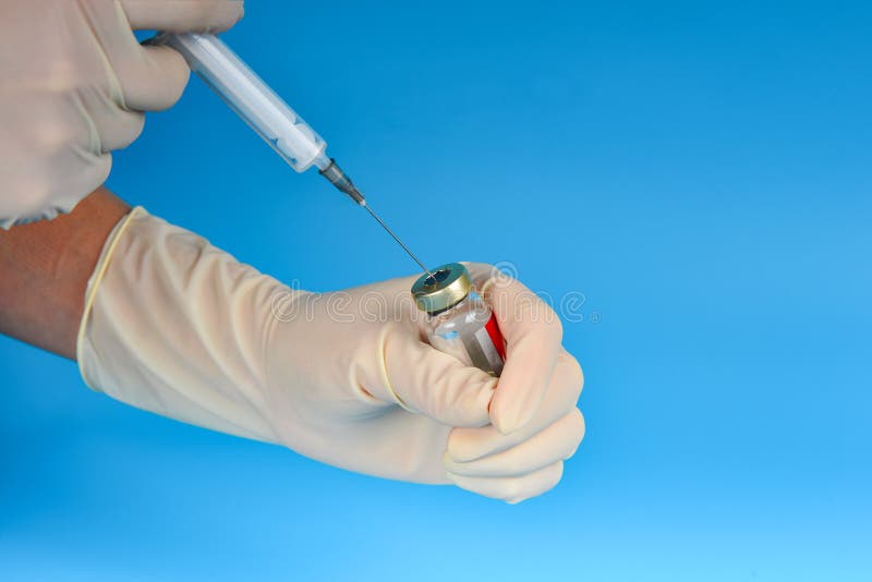 A doctor in medical gloves is taking medicine from a vial on a blue background into a syringe stock photo A doctor in medical gloves is taking medicine from a vial on a blue background into a syringe stock photo