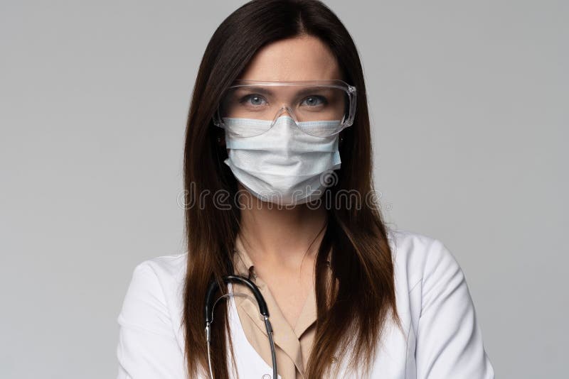 Doctor / nurse smiling behind surgeon mask. Closeup portrait of young caucasian woman model in white medical scrub