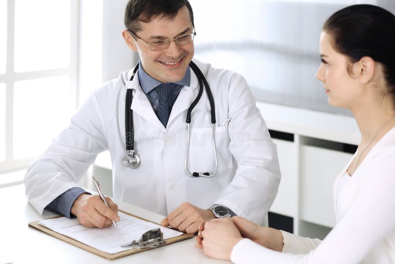 Doctor and patient discussing medical exam resoults at hospital office. Physician using clipboard for filling up royalty free stock image