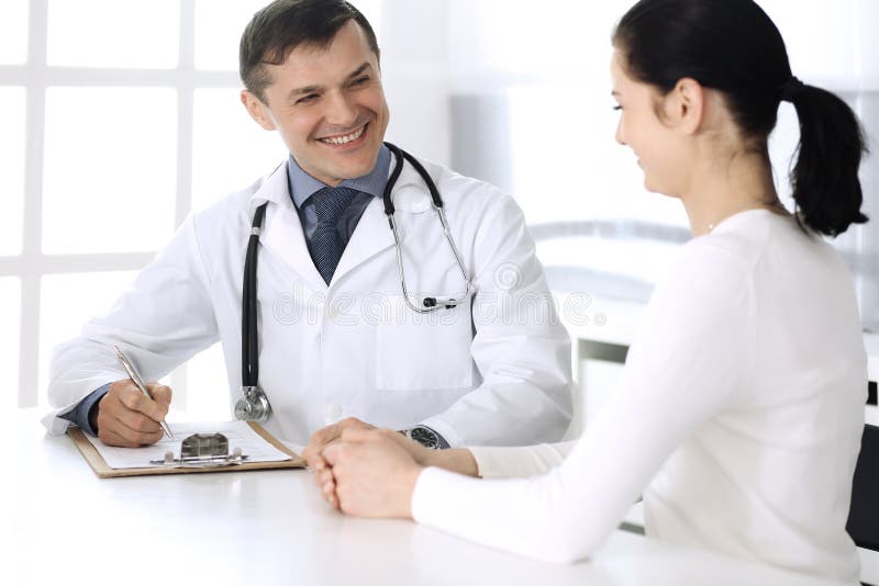 Doctor and patient discussing medical exam resoults at hospital office. Physician using clipboard for filling up stock photo