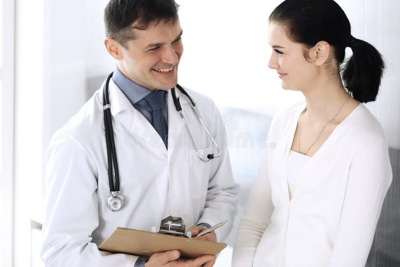 Doctor and patient discussing medical exam resoults at hospital office. Physician using clipboard for filling up royalty free stock photo