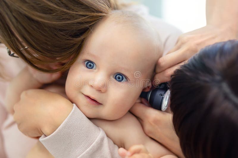 Doctor pediatrist examining childs ear with otoscope. Mom holding baby with hands. Medicine, healthcare ,pediatry and people.