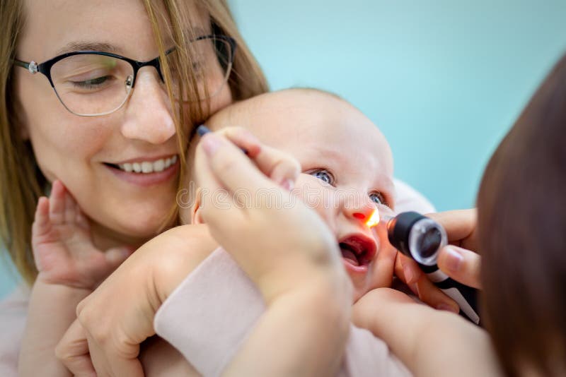 Doctor pediatrist examining childs nose with otoscope. Mom holding baby with hands while health checkup. Medicine