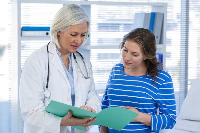Doctor que muestra informe médico a la mujer embarazada imagenes de archivo Doctor que muestra informe médico a la mujer embarazada imagenes de archivo