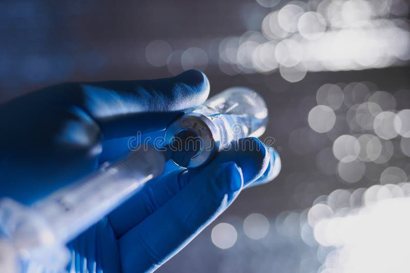 A Doctor`s hand in blue medical gloves holding syringe and vaccine.