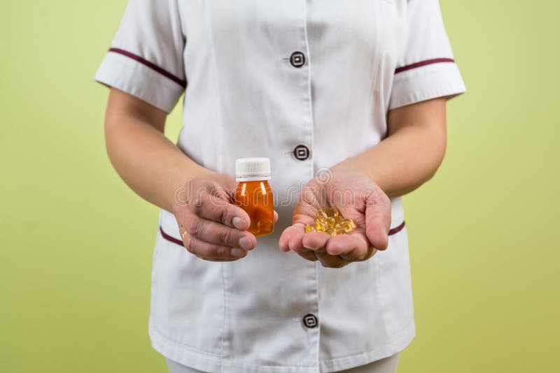 Doctor`s hands hold pills in an orange jar. Tablets or vitamins in the hands of a doctor. The concept of health, medicine