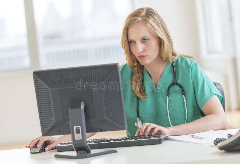 Doctor In Scrubs Using Computer At Hospital Desk royalty free stock photography Doctor In Scrubs Using Computer At Hospital Desk royalty free stock photography