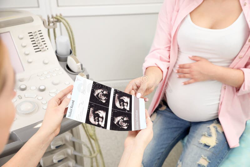 Doctor showing ultrasound images of baby to future mother in clinic stock image Doctor showing ultrasound images of baby to future mother in clinic stock image