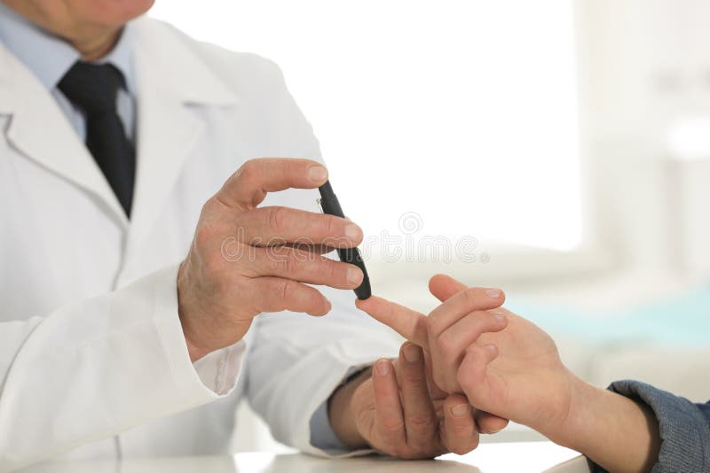 Doctor taking patient`s blood sample with lancet pen in hospital. Diabetes control
