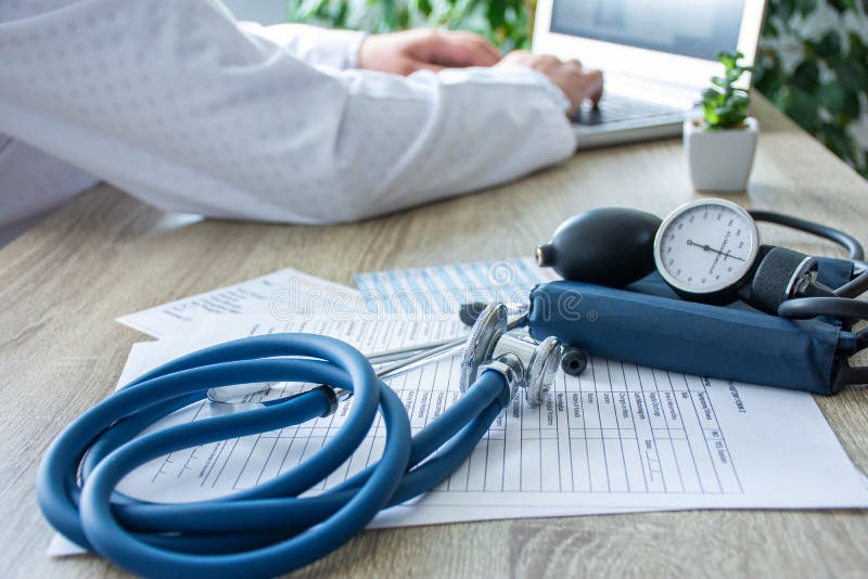 Doctor at work on the computer in the blurry background, in the foreground - a stethoscope with sphygmomanometer on medical docume stock photos
