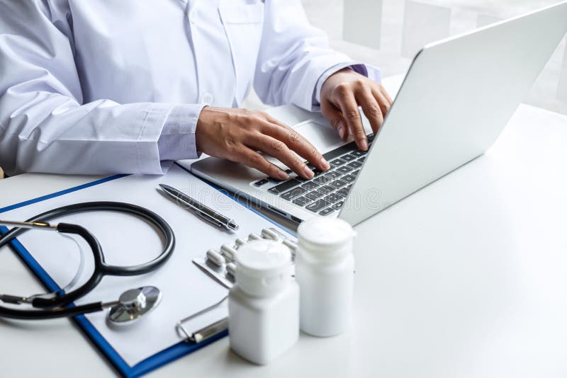 Doctor working with laptop in hospital and medical stethoscope, medicine on clipboard on desk stock photo Doctor working with laptop in hospital and medical stethoscope, medicine on clipboard on desk stock photo