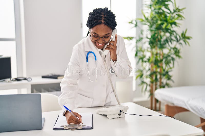 Doctora afroamericana hablando en un smartphone escribiendo documentos en la clínica imagenes de archivo