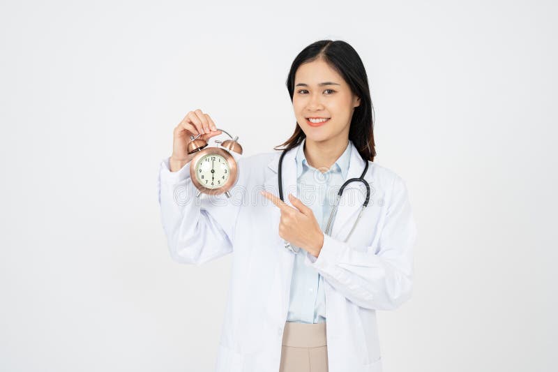 Doctora femenina sonriendo y aguantando el reloj. aislado en fondo blanco fotografía de archivo