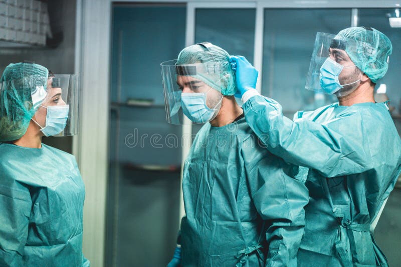 Doctors and nurse preparing to work in hospital for surgical operation during coronavirus pandemic outbreak - Medical workers getting dressed inside clinic - Focus on left men faces