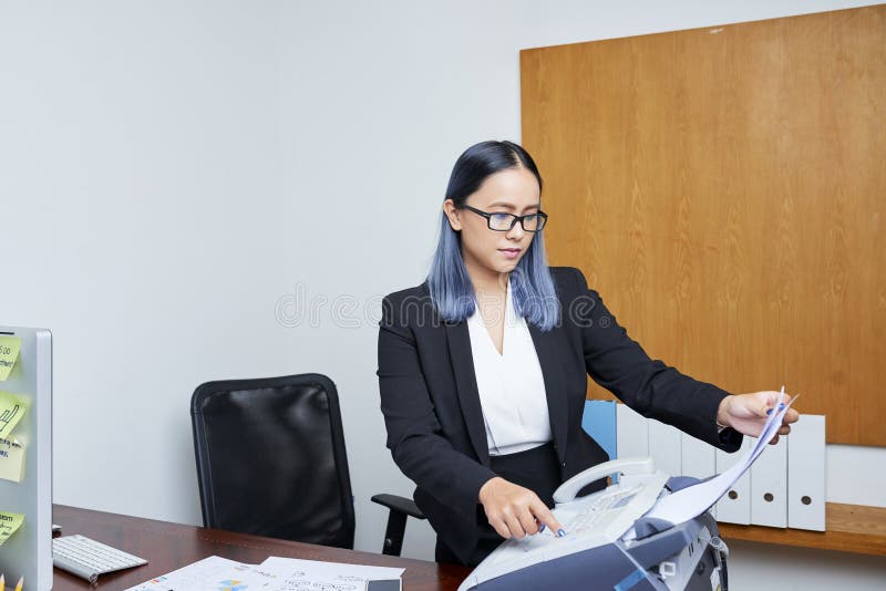 Young Asian businesswoman with blue hair printing out document via fax machine. Young Asian businesswoman with blue hair printing out document via fax machine