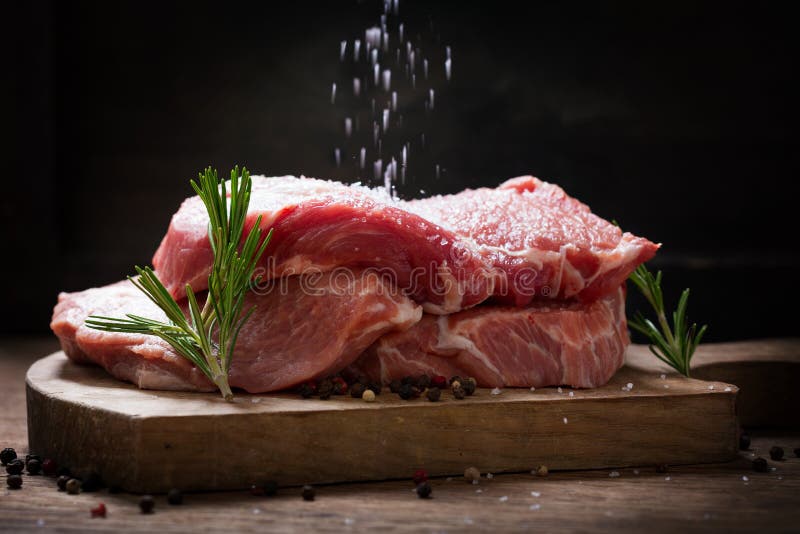 Dodanie soli do świeżego mięsa wieprzowego z rozmarynem i przyprawami obrazy stock