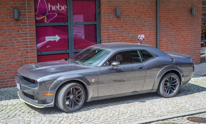 Popular dark grey American sporting car Dodge Challenger copue with two doors eparked on a street. Left side and front view with grill and logo. Popular dark grey American sporting car Dodge Challenger copue with two doors eparked on a street. Left side and front view with grill and logo.