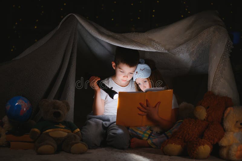 Doi copii cu lanternă citesc o carte sub o pătură ca un cort royalty free stock photography