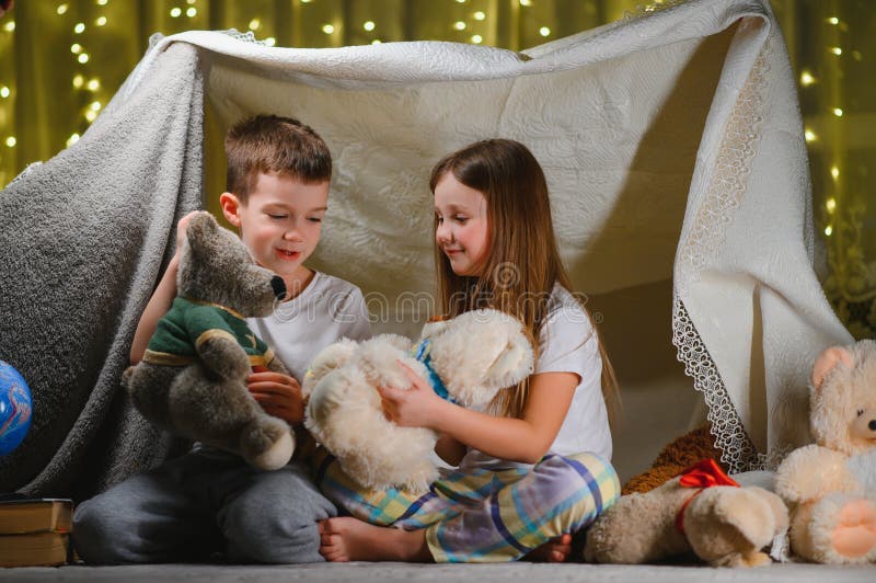 Doi copii mici se joacă acasă seara pentru a construi un cort de camping pentru a citi cărți cu lanternă și a dormi înăuntru. conc stock photography