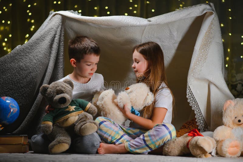 Doi copii mici se joacă acasă seara pentru a construi un cort de camping pentru a citi cărți cu lanternă și a dormi înăuntru. conc royalty free stock images