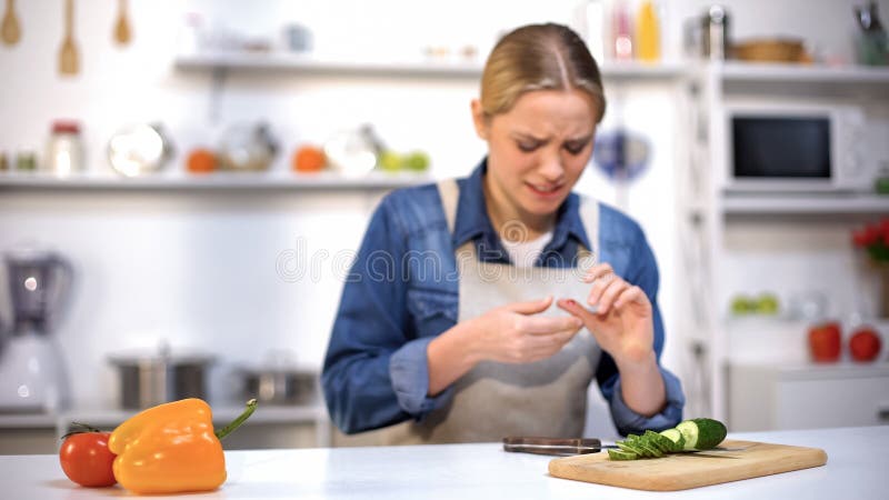 Doigt coupé femelle tout en coupant en tranches le concombre, accident dans la cuisine, blessure de ménage