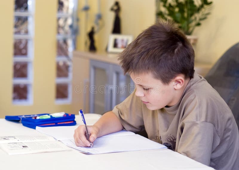 Chlapec sedí za stolom v obývacej izbe, robí svoju domácu úlohu.