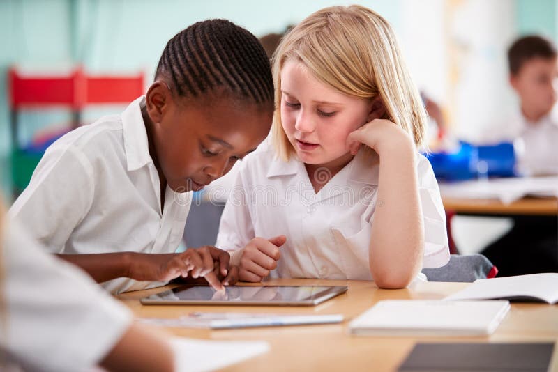 Dois alunos da escola primária que vestem o uniforme usando a tabuleta de Digitas na mesa