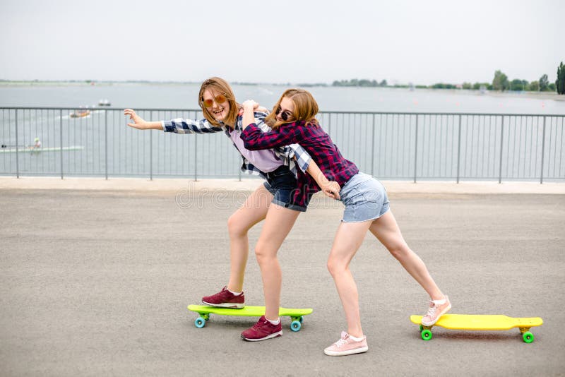 Dois amigos fêmeas de sorriso que aprendem o longboard de montada com ajuda de Conceito da amizade fotografia de stock royalty free Dois amigos fêmeas de sorriso que aprendem o longboard de montada com ajuda de Conceito da amizade fotografia de stock royalty free