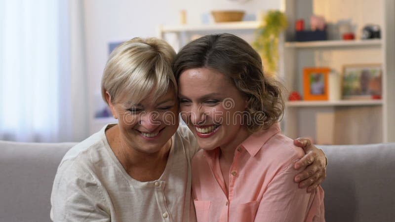 Dois amigos fêmeas que riem no sofá, bisbilhotice e tendo o divertimento junto, lento-mo