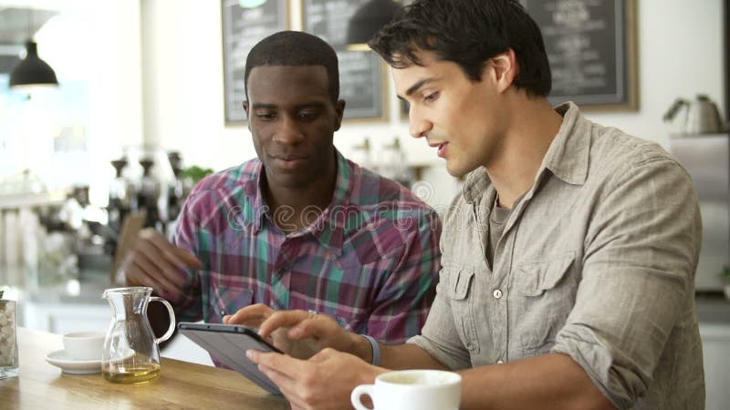 Dois amigos masculinos na cafetaria que olha a tabuleta de Digitas