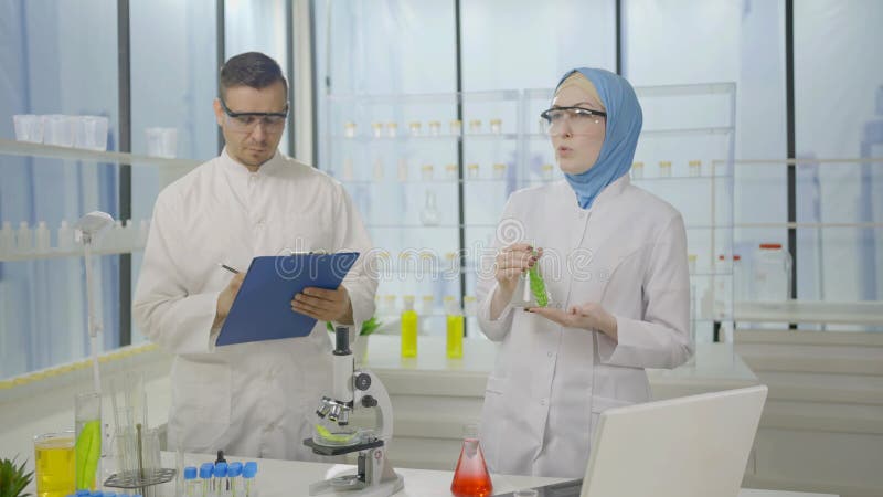 Dois cientistas muçulmanos em casacos de laboratório num laboratório moderno estão conversando