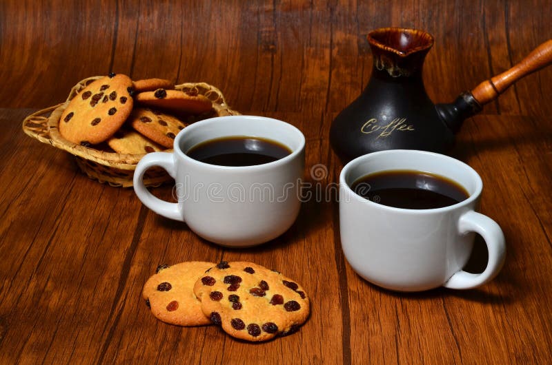 Dois copos do café preto com as cookies americanas friáveis e um fabricante de café turco da argila no fundo de madeira do marrom fotografia de stock Dois copos do café preto com as cookies americanas friáveis e um fabricante de café turco da argila no fundo de madeira do marrom fotografia de stock