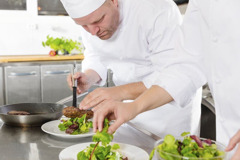 Dois cozinheiros chefe preparam o prato do bife no restaurante gourmet fotografia de stock royalty free Dois cozinheiros chefe preparam o prato do bife no restaurante gourmet fotografia de stock royalty free
