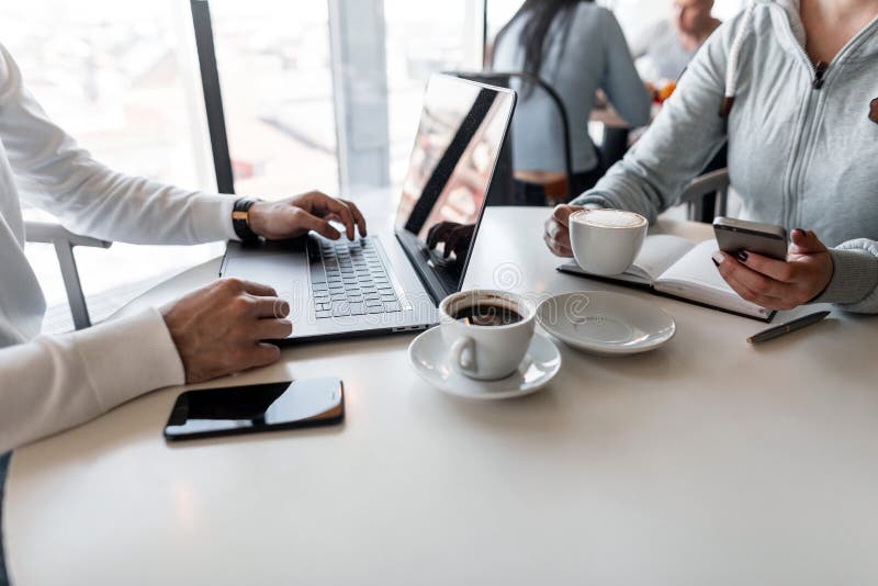 Dois desenhistas bem sucedidos novos estão sentando-se com um portátil com um bloco de notas que discutem um projeto criativo e q fotos de stock Dois desenhistas bem sucedidos novos estão sentando-se com um portátil com um bloco de notas que discutem um projeto criativo e q fotos de stock