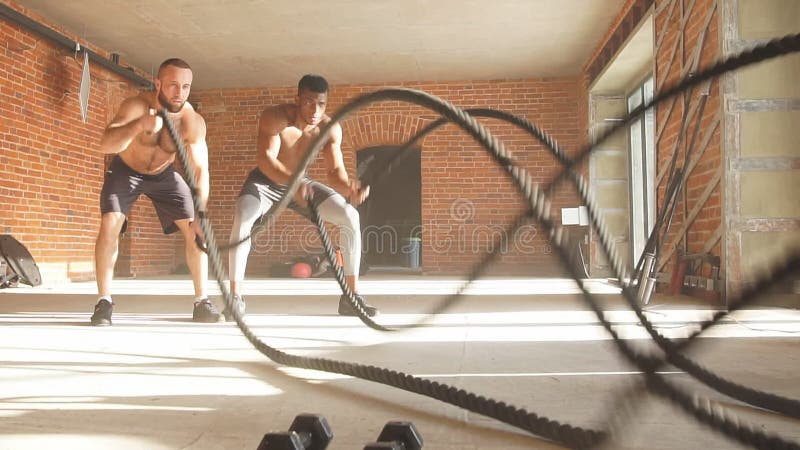 Dois desportistas desencapados multi-étnicos da caixa que exercitam com cordas da batalha no gym Movimento lento