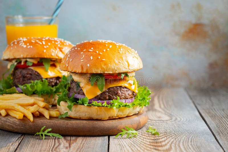 Dois hamburgueres caseiros frescos com batatas e suco de laranja fritados em uma tabela de madeira Com espaço da cópia imagem de stock royalty free Dois hamburgueres caseiros frescos com batatas e suco de laranja fritados em uma tabela de madeira Com espaço da cópia imagem de stock royalty free